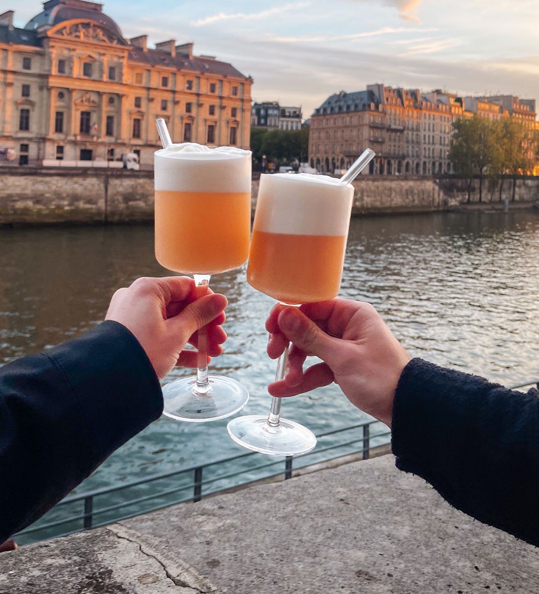 Deux cocktails sour levés devant la Seine au coucher du soleil